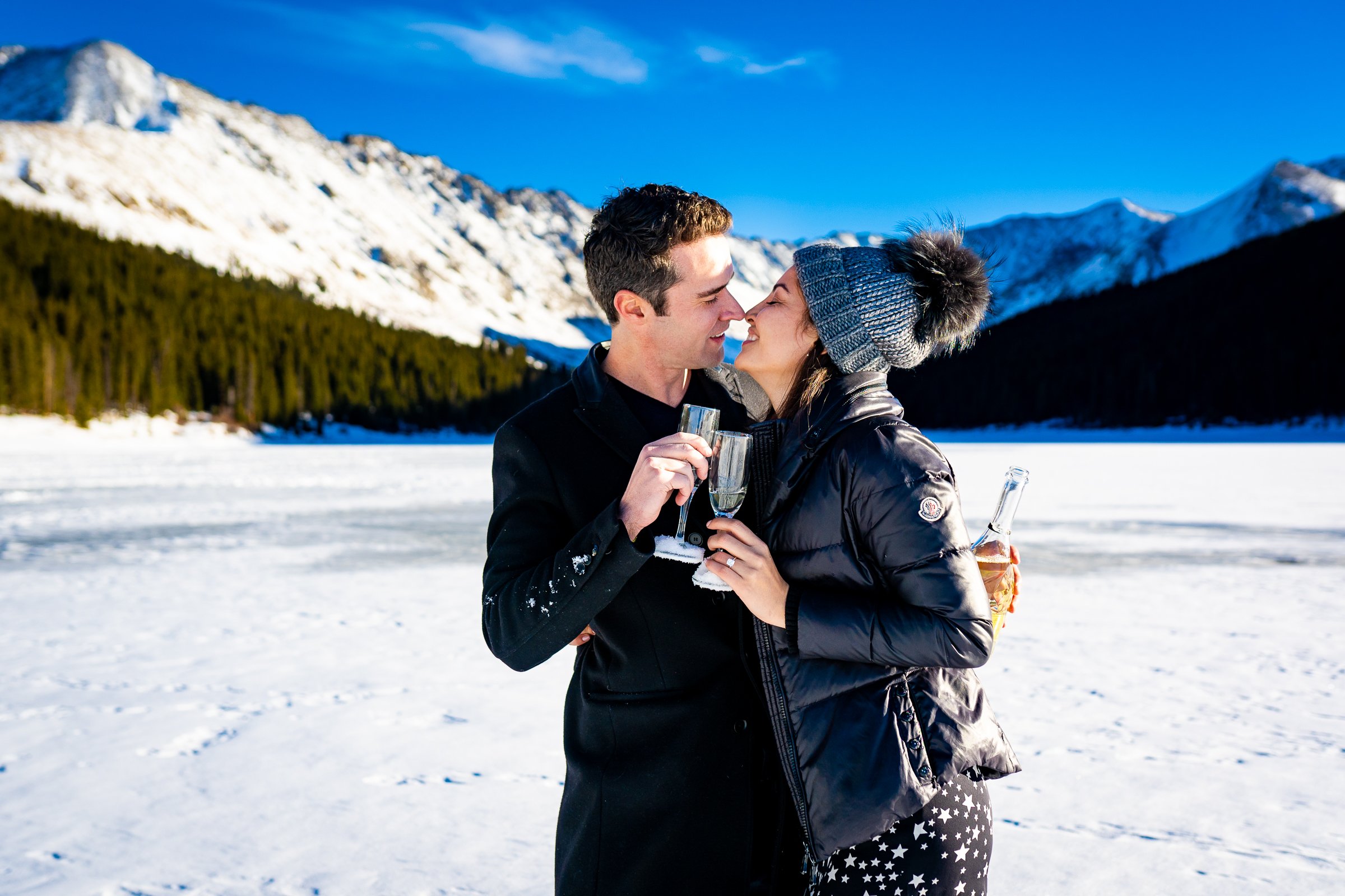 Engaged couple celebrates proposal with champagne on frozen lake with snowcapped mountains in the background, Engagement Session, Engagement Photos, Engagement Photos Inspiration, Engagement Photography, Engagement Photographer, Winter Engagement Photos, Proposal Photos, Proposal Photographer, Proposal Photography, Winter Proposal, Mountain Proposal, Proposal Inspiration, Summit County engagement session, Summit County engagement photos, Summit County engagement photography, Summit County engagement photographer, Summit County engagement inspiration, Colorado engagement session, Colorado engagement photos, Colorado engagement photography, Colorado engagement photographer, Colorado engagement inspiration, Clinton Gulch Engagement