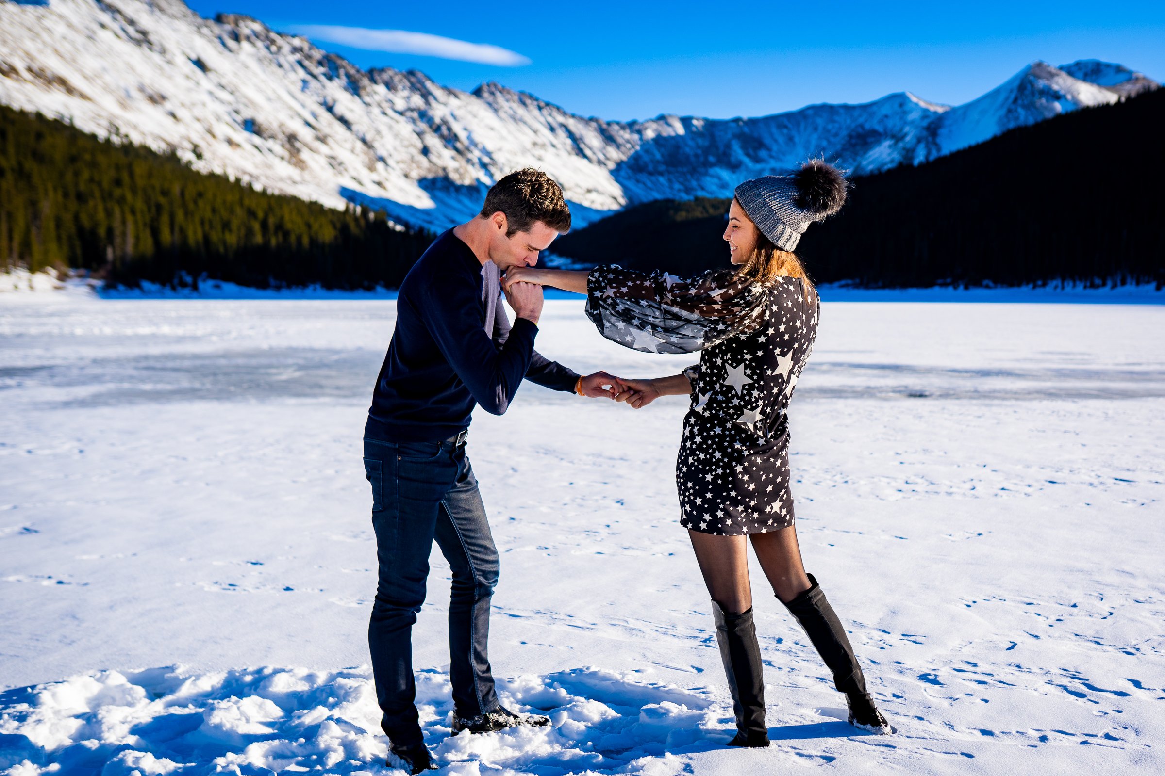 Newly engaged couple celebrate their proposal with a kiss on a frozen lake with snowcapped mountains in the background, Engagement Session, Engagement Photos, Engagement Photos Inspiration, Engagement Photography, Engagement Photographer, Winter Engagement Photos, Proposal Photos, Proposal Photographer, Proposal Photography, Winter Proposal, Mountain Proposal, Proposal Inspiration, Summit County engagement session, Summit County engagement photos, Summit County engagement photography, Summit County engagement photographer, Summit County engagement inspiration, Colorado engagement session, Colorado engagement photos, Colorado engagement photography, Colorado engagement photographer, Colorado engagement inspiration, Clinton Gulch Engagement