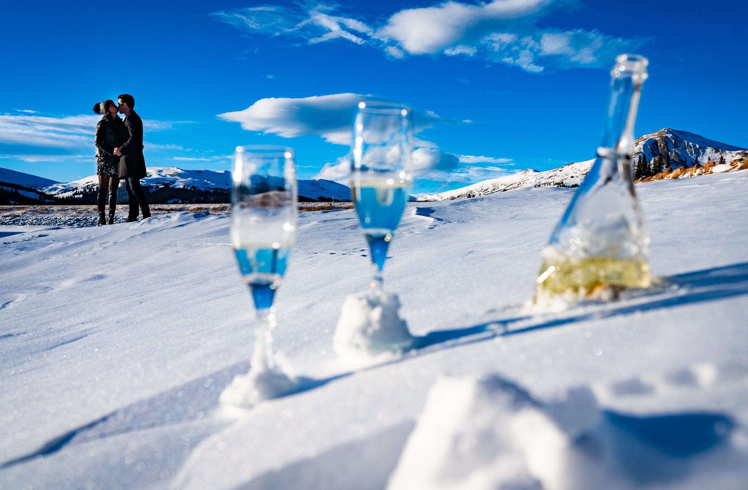 Engaged couple celebrates proposal with champagne on frozen lake with snowcapped mountains in the background, Engagement Session, Engagement Photos, Engagement Photos Inspiration, Engagement Photography, Engagement Photographer, Winter Engagement Photos, Proposal Photos, Proposal Photographer, Proposal Photography, Winter Proposal, Mountain Proposal, Proposal Inspiration, Summit County engagement session, Summit County engagement photos, Summit County engagement photography, Summit County engagement photographer, Summit County engagement inspiration, Colorado engagement session, Colorado engagement photos, Colorado engagement photography, Colorado engagement photographer, Colorado engagement inspiration, Clinton Gulch Engagement