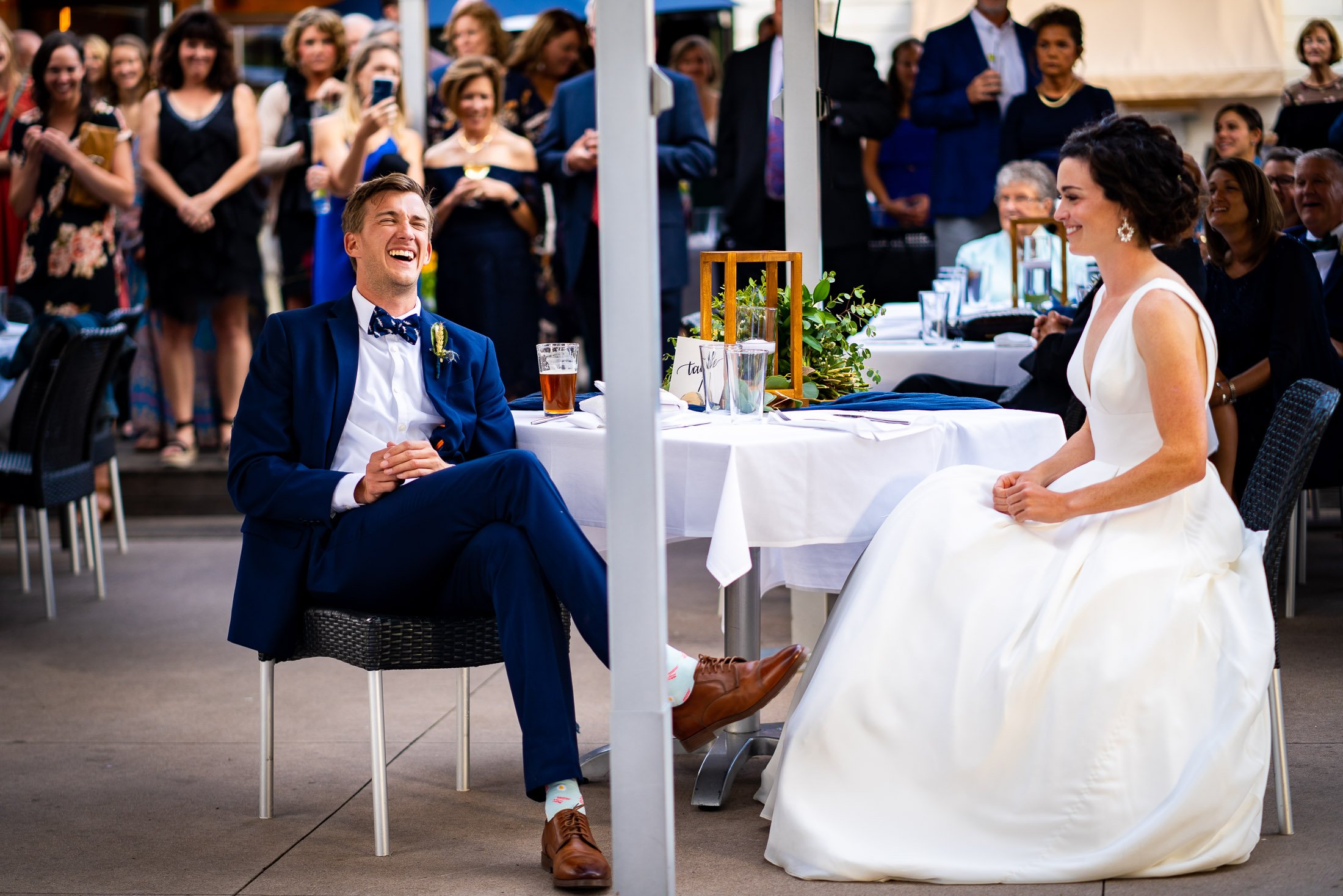 Bride and groom react to reception speeches while sitting on outdoor patio during the wedding reception, wedding, wedding photos, wedding photography, wedding photographer, wedding inspiration, wedding photo inspiration, wedding portraits, wedding ceremony, wedding reception, mountain wedding, Catholic Church wedding, Catholic Church wedding photos, Catholic Church wedding photography, Catholic Church wedding photographer, Catholic Church wedding inspiration, Catholic Church wedding venue, Steamboat Springs wedding, Steamboat Springs wedding photos, Steamboat Springs wedding photography, Steamboat Springs wedding photographer, Colorado wedding, Colorado wedding photos, Colorado wedding photography, Colorado wedding photographer, Colorado mountain wedding, Colorado wedding inspiration