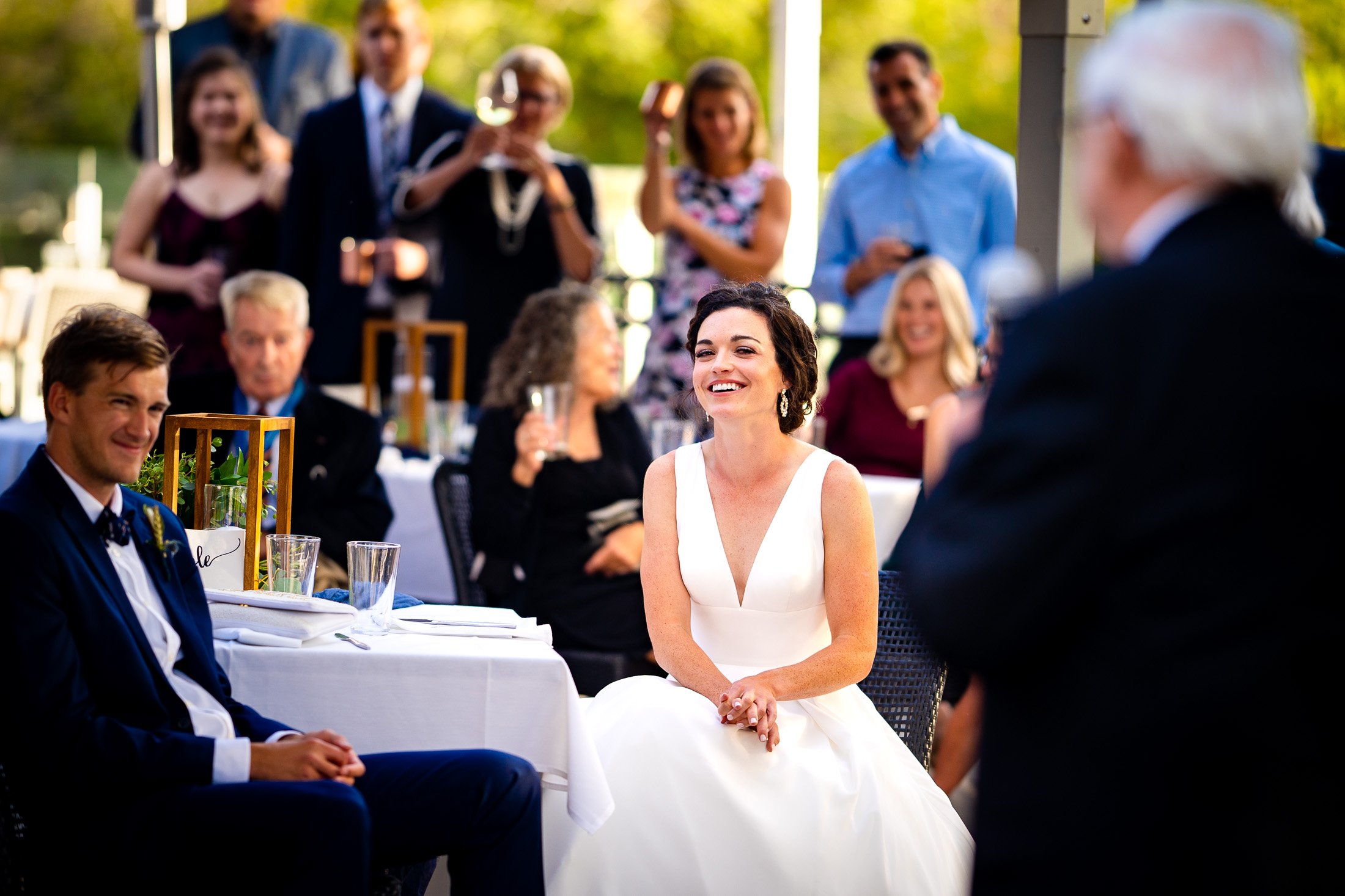 Bride and groom react to reception speeches while sitting on outdoor patio during the wedding reception, wedding, wedding photos, wedding photography, wedding photographer, wedding inspiration, wedding photo inspiration, wedding portraits, wedding ceremony, wedding reception, mountain wedding, Catholic Church wedding, Catholic Church wedding photos, Catholic Church wedding photography, Catholic Church wedding photographer, Catholic Church wedding inspiration, Catholic Church wedding venue, Steamboat Springs wedding, Steamboat Springs wedding photos, Steamboat Springs wedding photography, Steamboat Springs wedding photographer, Colorado wedding, Colorado wedding photos, Colorado wedding photography, Colorado wedding photographer, Colorado mountain wedding, Colorado wedding inspiration