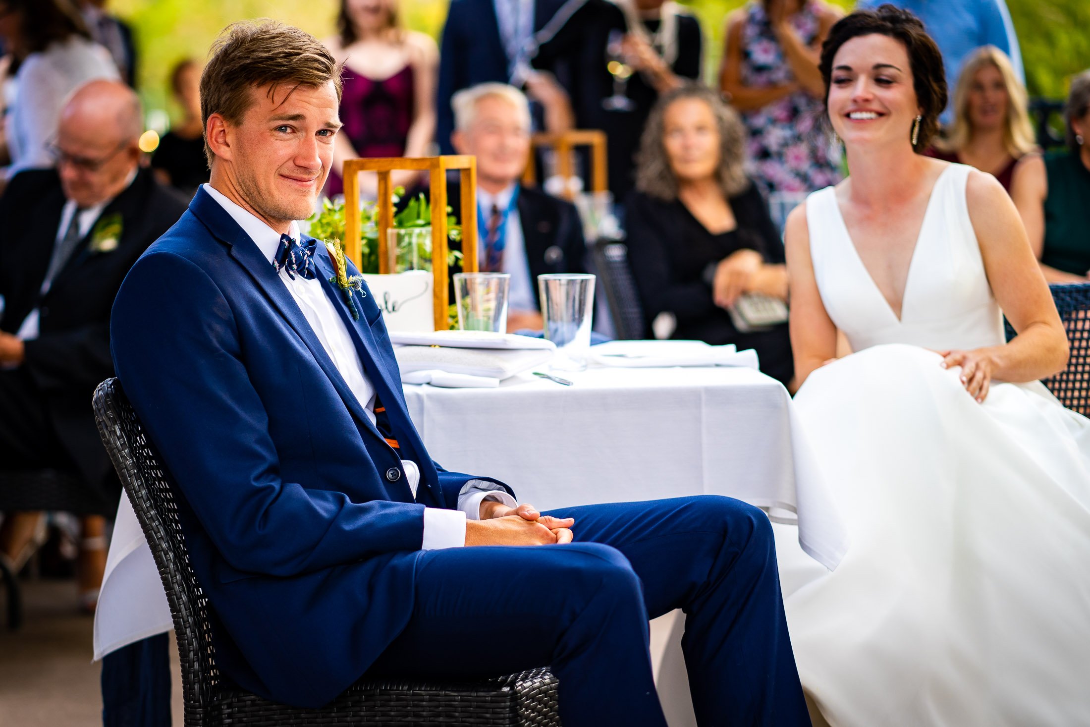 Bride and groom react to reception speeches while sitting on outdoor patio during the wedding reception, wedding, wedding photos, wedding photography, wedding photographer, wedding inspiration, wedding photo inspiration, wedding portraits, wedding ceremony, wedding reception, mountain wedding, Catholic Church wedding, Catholic Church wedding photos, Catholic Church wedding photography, Catholic Church wedding photographer, Catholic Church wedding inspiration, Catholic Church wedding venue, Steamboat Springs wedding, Steamboat Springs wedding photos, Steamboat Springs wedding photography, Steamboat Springs wedding photographer, Colorado wedding, Colorado wedding photos, Colorado wedding photography, Colorado wedding photographer, Colorado mountain wedding, Colorado wedding inspiration