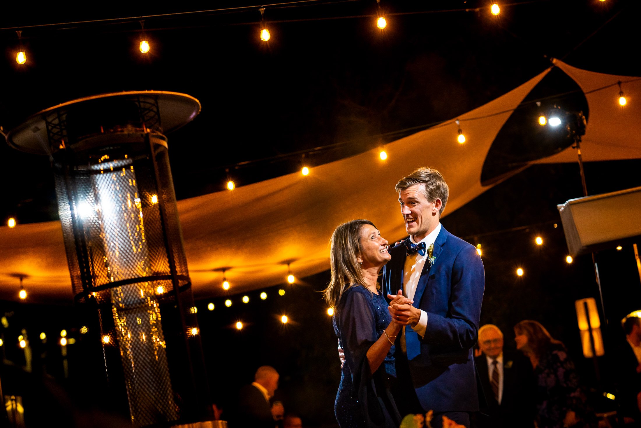 Groom shares a first dance with his mother on the outdoor patio under cafe lights at blue hour during their wedding reception, wedding, wedding photos, wedding photography, wedding photographer, wedding inspiration, wedding photo inspiration, wedding portraits, wedding ceremony, wedding reception, mountain wedding, Catholic Church wedding, Catholic Church wedding photos, Catholic Church wedding photography, Catholic Church wedding photographer, Catholic Church wedding inspiration, Catholic Church wedding venue, Steamboat Springs wedding, Steamboat Springs wedding photos, Steamboat Springs wedding photography, Steamboat Springs wedding photographer, Colorado wedding, Colorado wedding photos, Colorado wedding photography, Colorado wedding photographer, Colorado mountain wedding, Colorado wedding inspiration