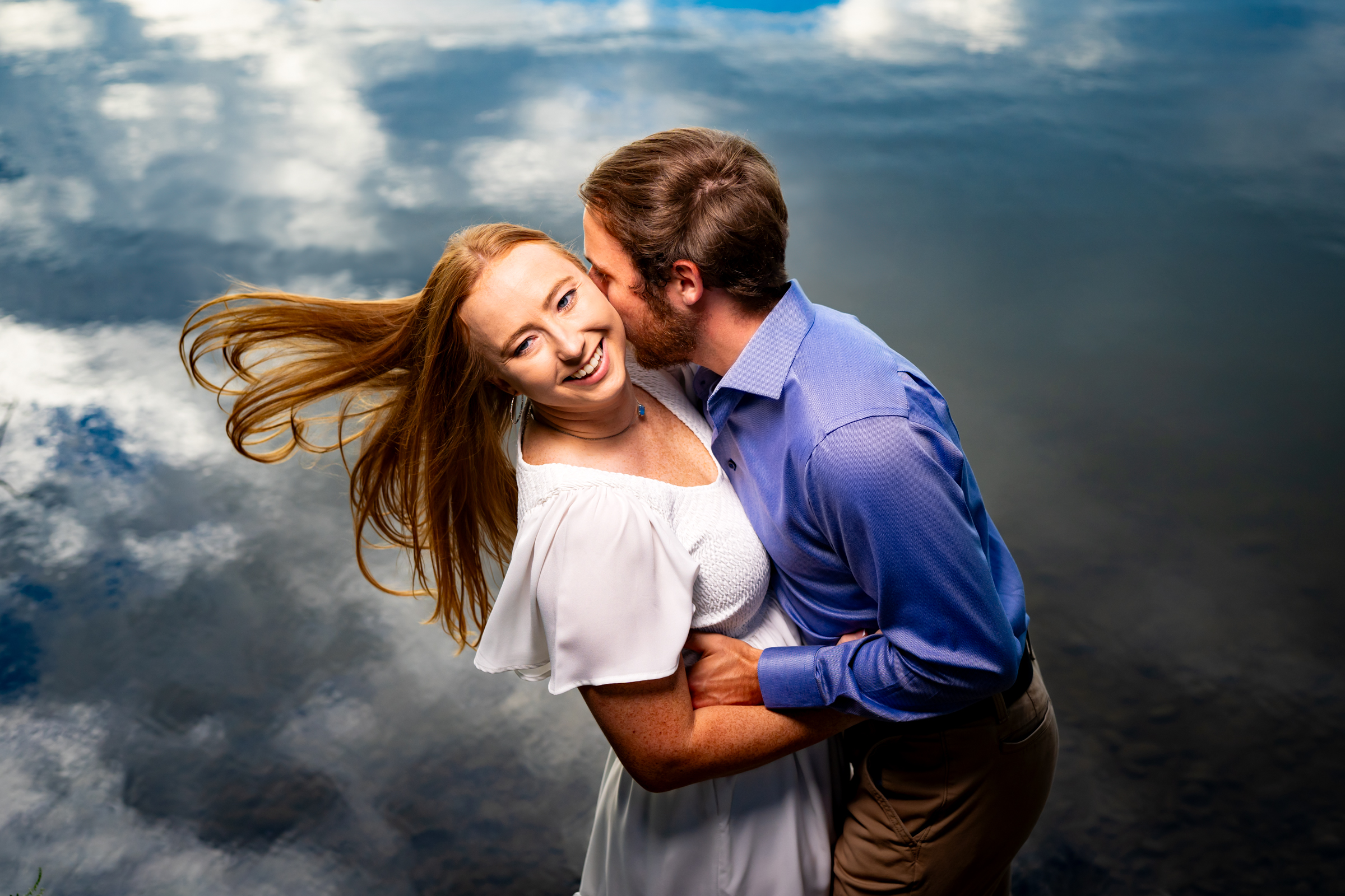 Engaged couple shares a kiss by the water at Golden Ponds in Longmont