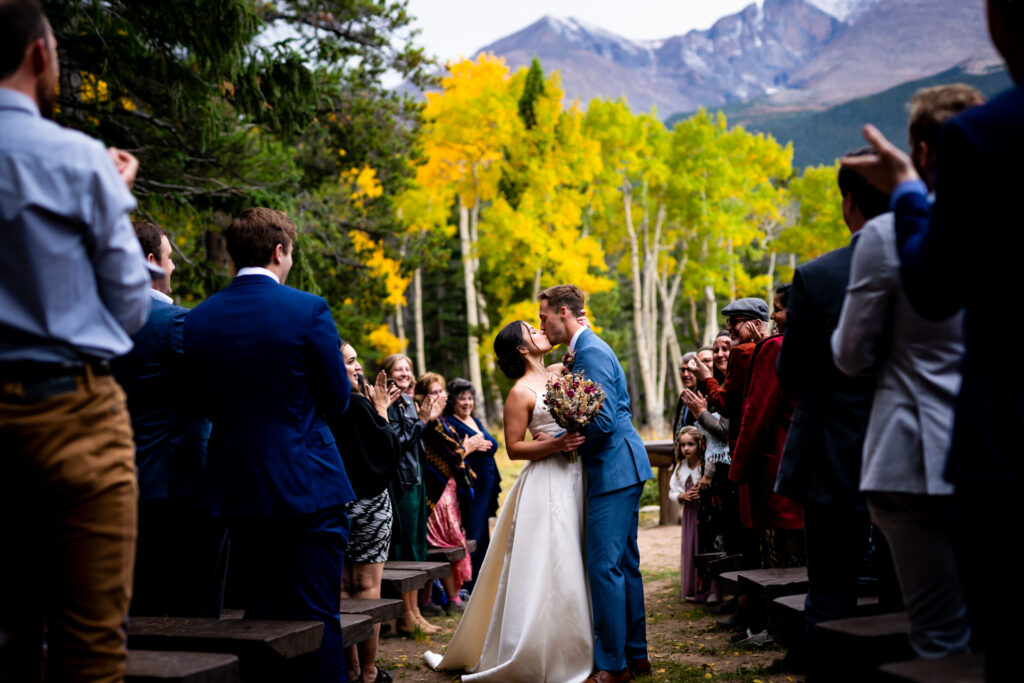 Bride and groom kiss as guests cheer during their recessional at their wedding ceremony