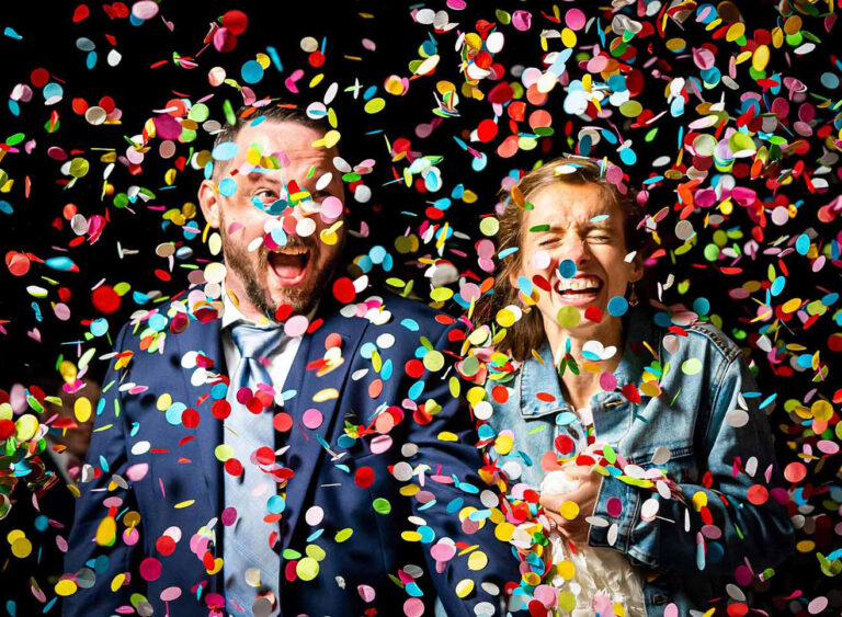 A bride and groom laugh during a confetti toss captured in a documentary wedding photography style