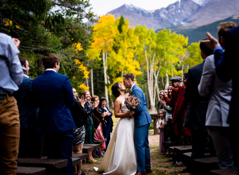 A bride and groom embrace for a kiss surrounded by their guests after getting married at the Dao House in Estes Park, Colorado